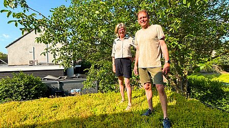 Karin en Peter staan tussen de sedumplantjes op het groene dak. op de achtegrond staat de walnotenboom in de tuin.