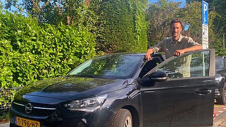 Olaf staat in de geopende deur van de deelauto