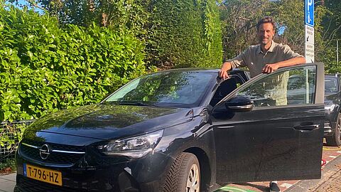 Olaf staat in de geopende deur van de deelauto