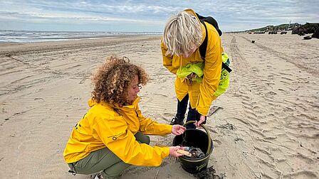 twee vrouwen stoppen zwerfafval in een emmer op het strand